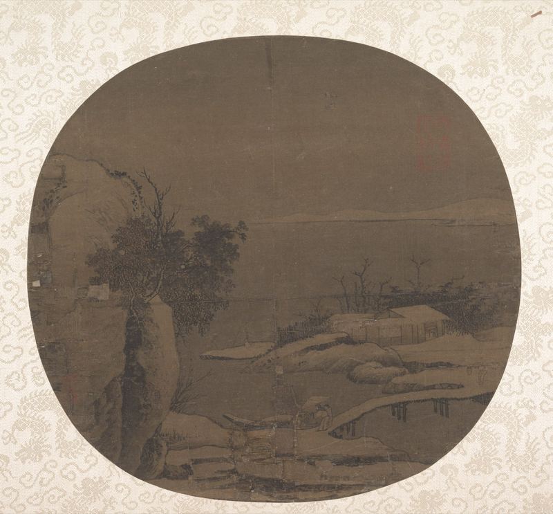 一幅深色绢本团扇，衬在浅色花纹的裱绫上。左边是一段长着斜树的岩岸；雪落在岸边低矮的屋顶、石头和一座小木桥上，宽阔平静的河面一直延伸到对岸隐约的山。