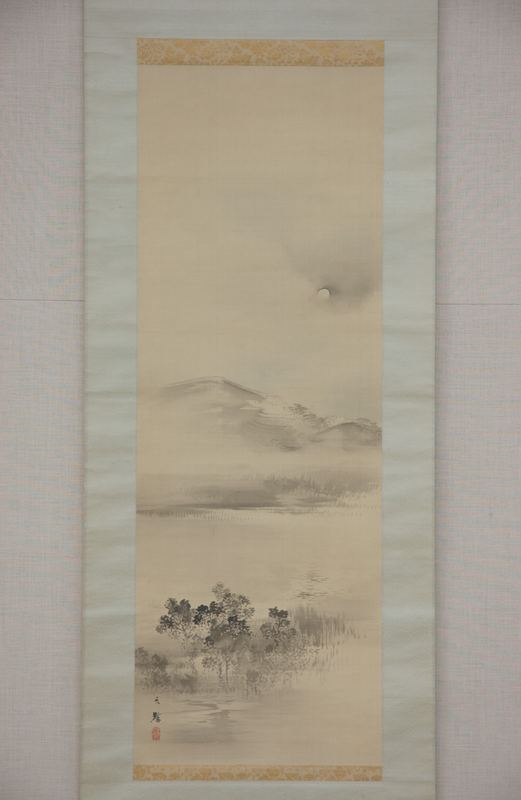 一幅淡色的绢本立轴：雾蒙蒙的天空里一轮淡淡的满月，下面是柔和的灰色山丘，中段横着一带低云，底部水边有几棵深色的树和一丛芦苇。